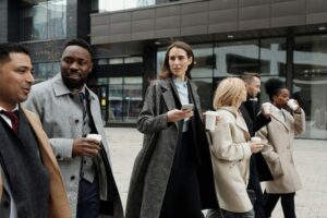ビジネス街を歩くスーツ姿の男女グループ。会話を交わしながらコーヒーを片手に通勤している様子が写っている。