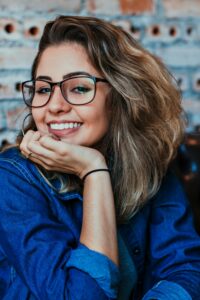 メガネをかけた女性が笑顔で頬杖をつき、リラックスした様子