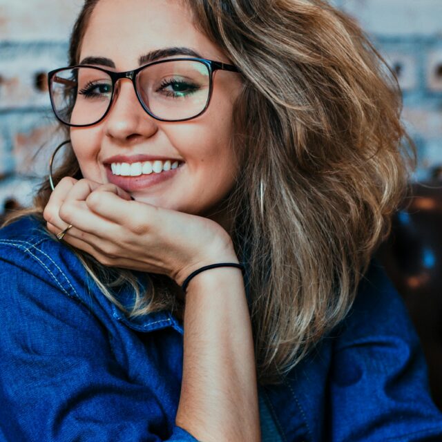 メガネをかけた女性が笑顔で頬杖をつき、リラックスした様子